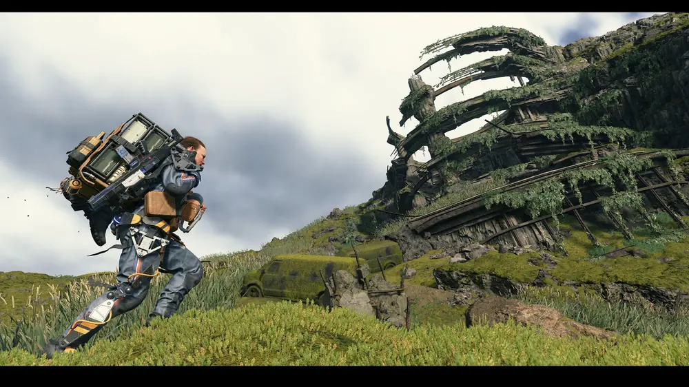 DEATH STRANDING: kurier z ładunkiem na plecach idzie zieloną skarpą w stronę porośniętej konstrukcji
